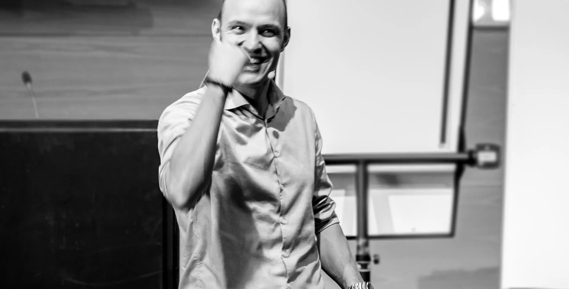 Ulrik Lynge midt i et foredrag med hånden i nakken, grinende.